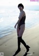 A woman in a bathing suit and thigh high boots on the beach.