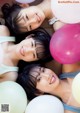 A group of young women laying on top of a bed with balloons.