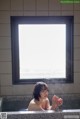 A woman sitting in a bathtub in front of a window.